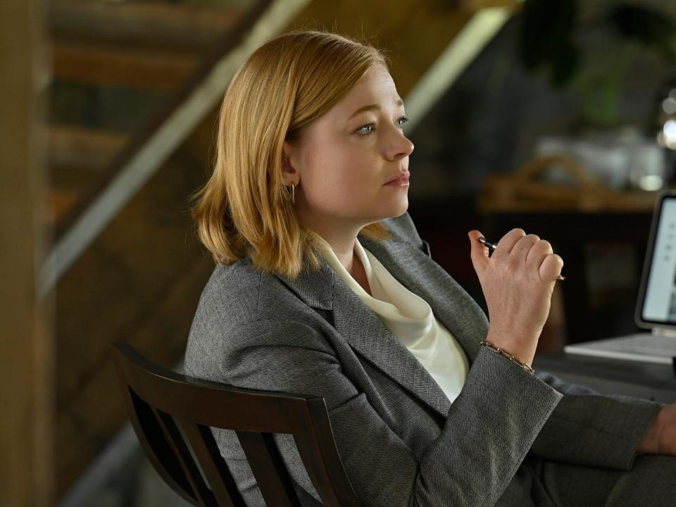 A white woman with sort strawberry-blonde/red hair wearing a grey suit.