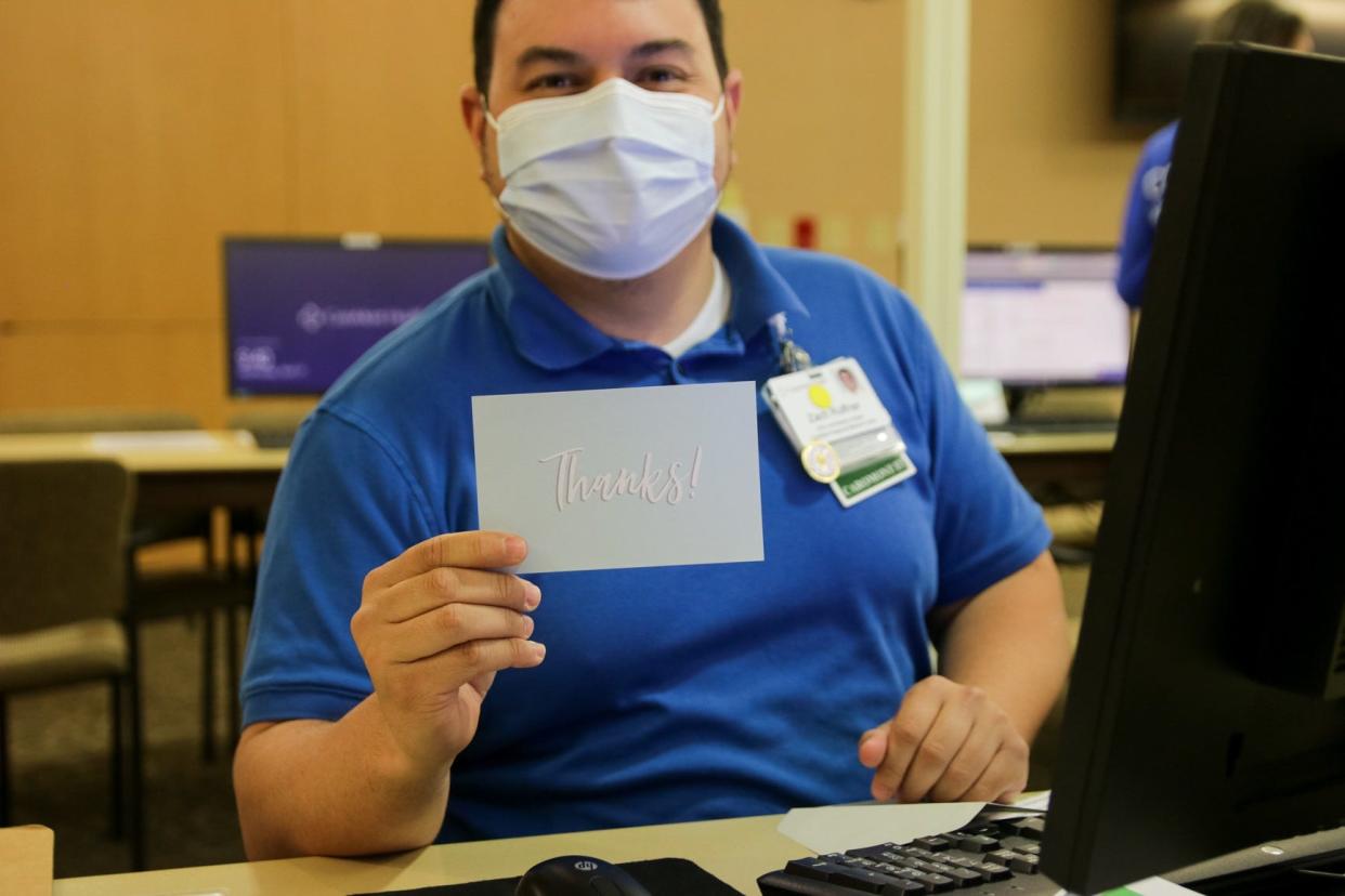 A CaroMont Health employee working at the COVID-19 vaccine clinic poses with a thank you card made and delivered by cadets of North Gaston High School's JROTC program.