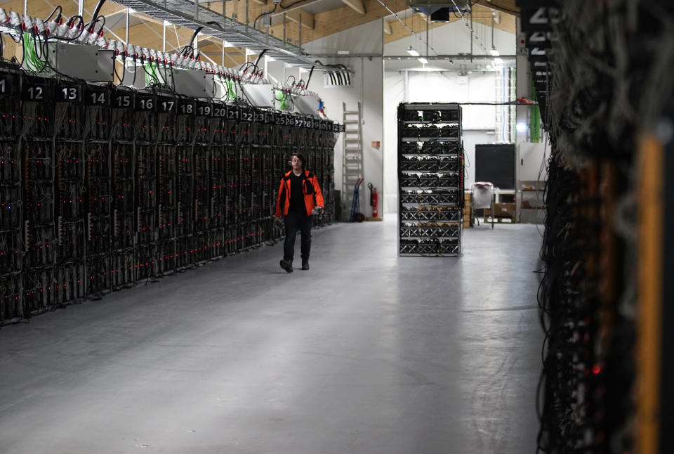 In this photo taken on Jan. 17, 2018, a worker walks along a row of computer rigs that run around the clock 'mining' bitcoin inside the Genesis Mining cryptocurrency mine in Keflavik, Iceland. Hand in hand with the rise of bitcoin is a soaring cost of “mining" the cryptocurrency. The energy demand has developed because of the soaring cost of producing the cryptocurrency, which requires computers solving math formulas to mine the 4.2 million coins still available. (AP Photos/Egill Bjarnason)