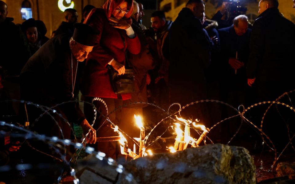 A priest lights a candle at a Christmas installation of a grotto with figures standing amid rubble surrounded by a razor wire, outside the Church of the Nativity, in support of Gaza, on Manger Square in Bethlehem, in the Israeli-occupied West Bank, December 23, 2023.