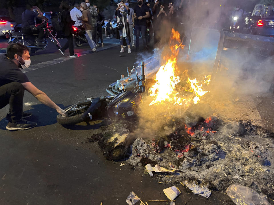 En esta imagen del lunes 19 de septiembre de 2022 tomada por una persona no empleada por Associated Press y obtenida por AP fuera de Irán, un hombre tira de una motocicleta policial incendiada durante una protesta por la muerte de una mujer que había sido detenida por incumplir el código de vestuario del país, en el centro de Teherán, Irán. (AP Foto)