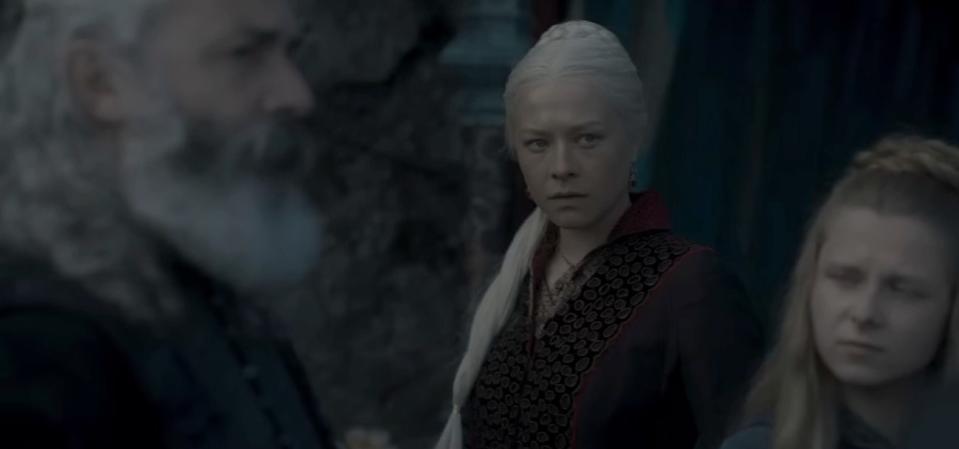 Rhaenyra stands behind an old man and a blonde woman