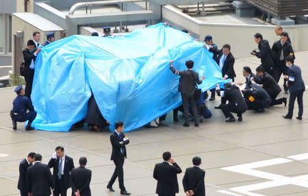 Police and security officers investigate an unidentified drone (under a blue cover) which was found on the rooftop of Prime Minister Shinzo Abe's official residence in Tokyo, in this photo taken by Kyodo April 22, 2015. Mandatory credit REUTERS/Kyodo