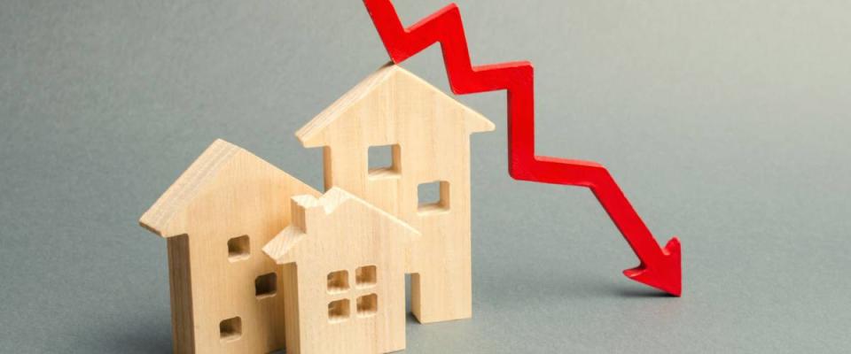 Miniature wooden houses and a red arrow down. The concept of falling interest rates.