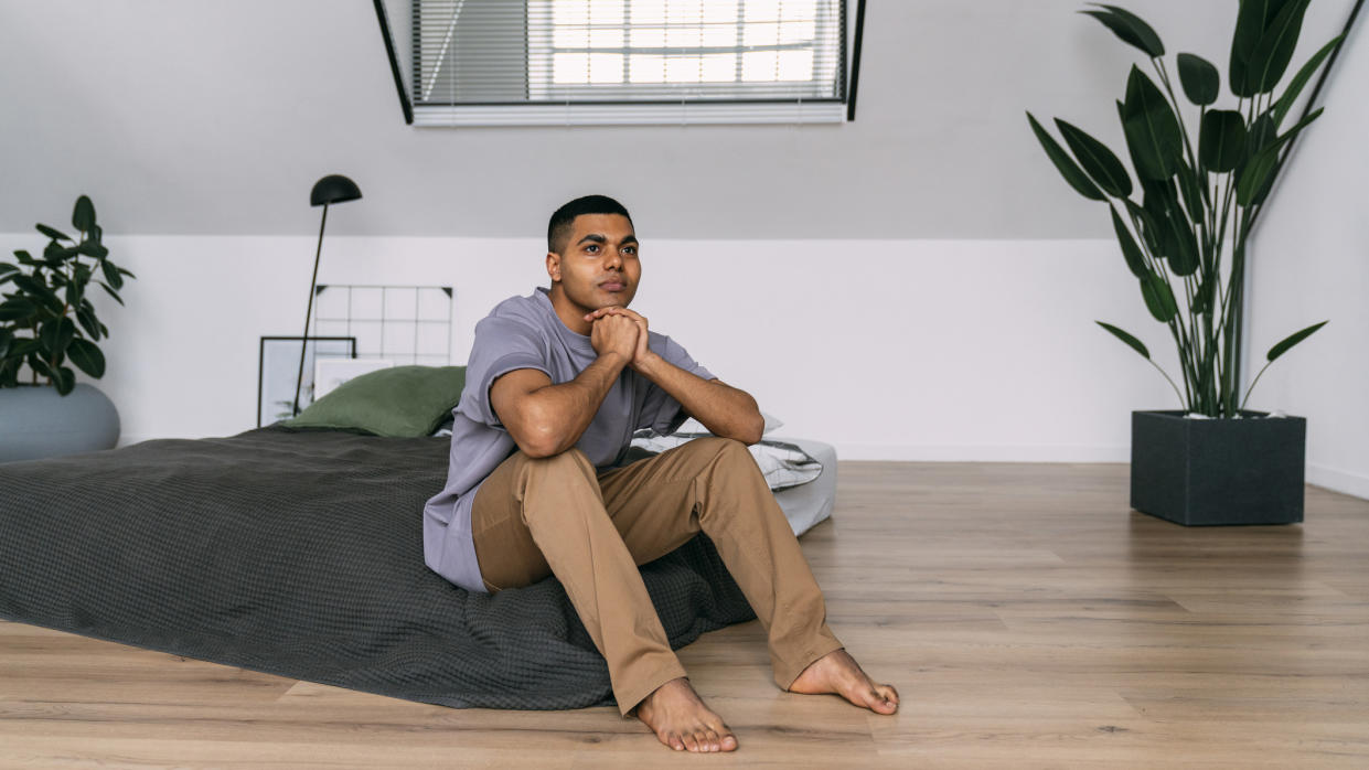  A man sits on a mattress on the floor before he falls asleep . 