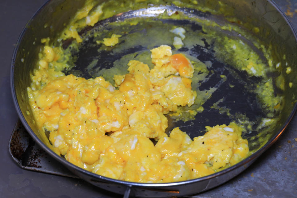 Scrambled eggs in a black pan, some eggs stick to the pan