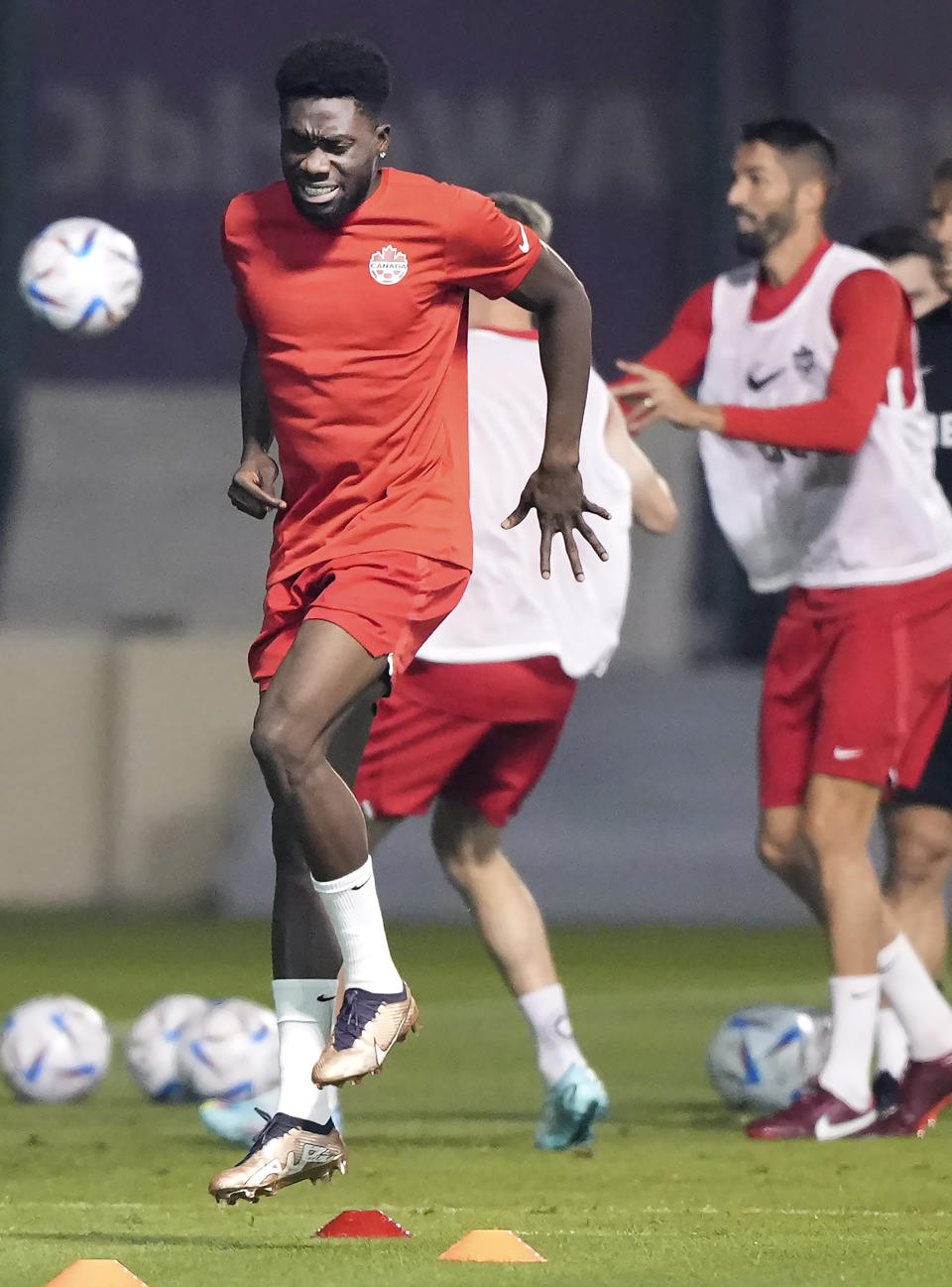 Canada star Alphonso Davies, left, grimaces during a warmup drill at the World Cup in Doha, Qatar, on Monday, Nov. 21, 2022. Davies, who is coming back from a hamstring strain, returned to the warmup. (Nathan Denette/The Canadian Press via AP)