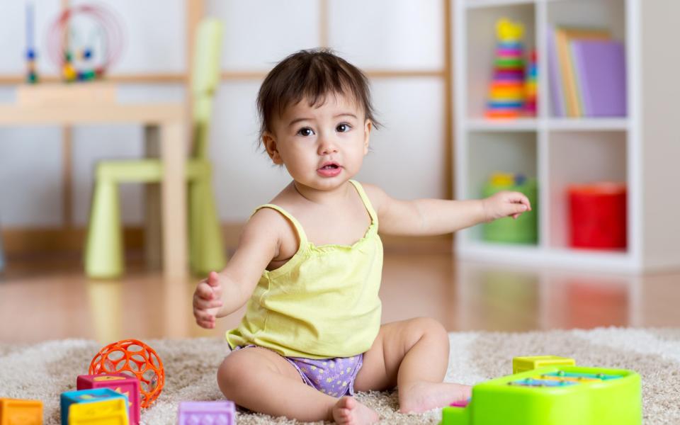 Toddler sitting among toys on carpet at home - Alamy Stock Photo