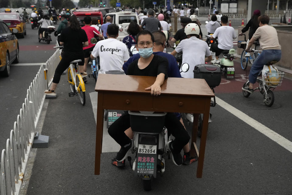 A man holds onto a table while on a bike in Beijing, Thursday, July 27, 2023. Chinese leader Xi Jinping's government is promising to drag the economy out of a crisis of confidence aggravated by tensions with Washington, wilting exports, job losses and anxiety among foreign companies about an expanded anti-spying law. (AP Photo/Ng Han Guan)