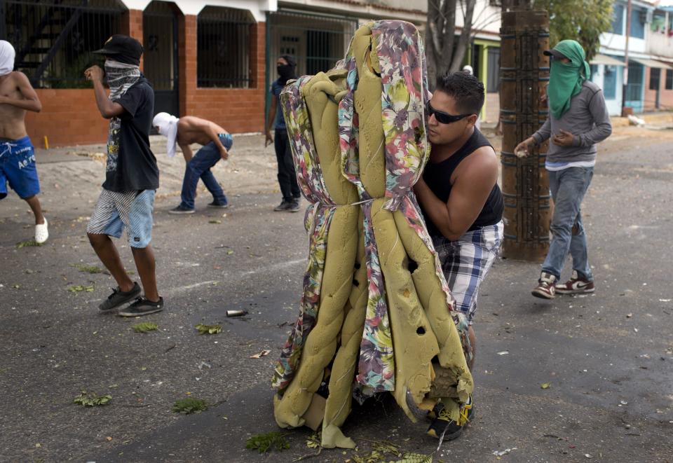 AP10ThingsToSee - A demonstrator protects himself with an old mattress during clashes with police during an anti-government protest in Valencia, Venezuela, Wednesday, Feb. 26, 2014. The protests began with students and were soon joined by others in several cities, upset over crime, economic problems and heavy-handed government response to the protests. (AP Photo/Rodrigo Abd, File)