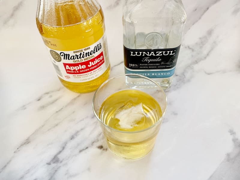 Glass of apple juice with ice next to bottles of Martinelli's Apple Juice and Lunazul Tequila.