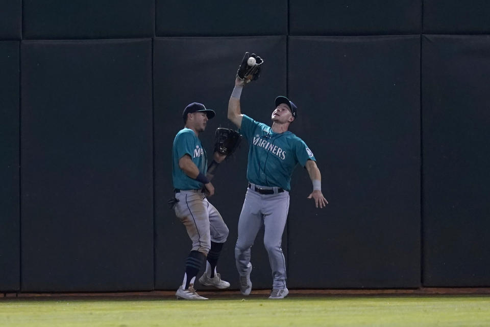 Seattle Mariners center fielder Jarred Kelenic, right, catches a flyout hit by Oakland Athletics' Yan Gomes next to left fielder Dylan Moore during the fourth inning of a baseball game in Oakland, Calif., Monday, Sept. 20, 2021. (AP Photo/Jeff Chiu)