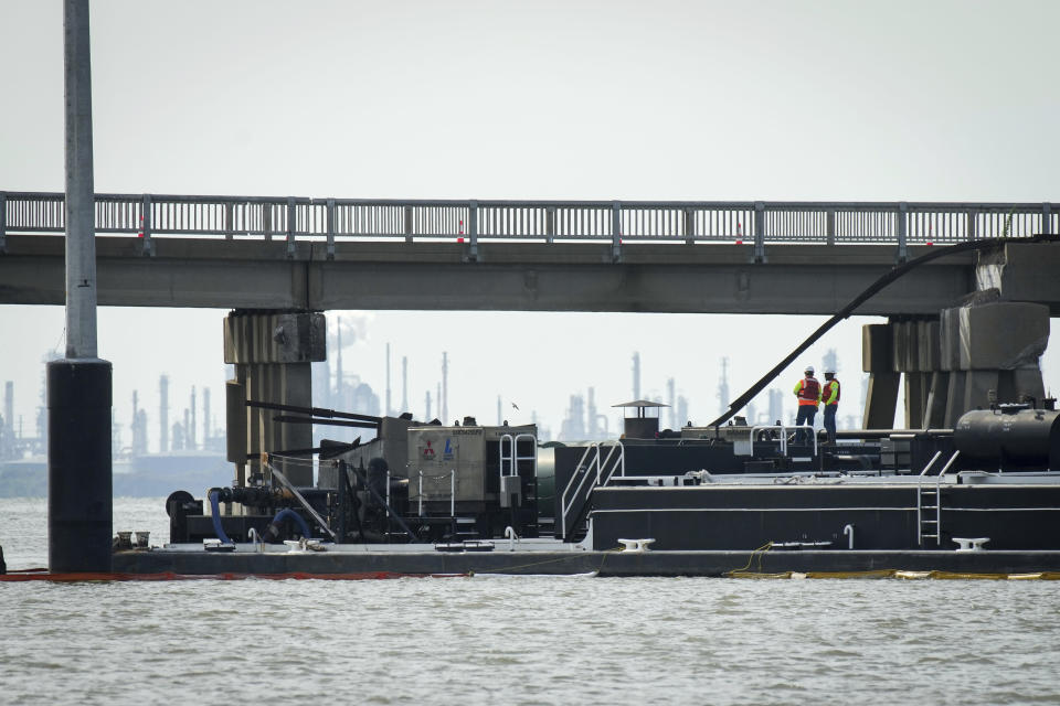 Two workers stand on the barge that struck the Pelican Island Bridge on Wednesday, May 15, 2024, in Galveston, Texas. The accident caused oil to spill into surrounding waters and closing the only road to a smaller and separate island that is home to a university, officials said. (Jon Shapley/Houston Chronicle via AP)