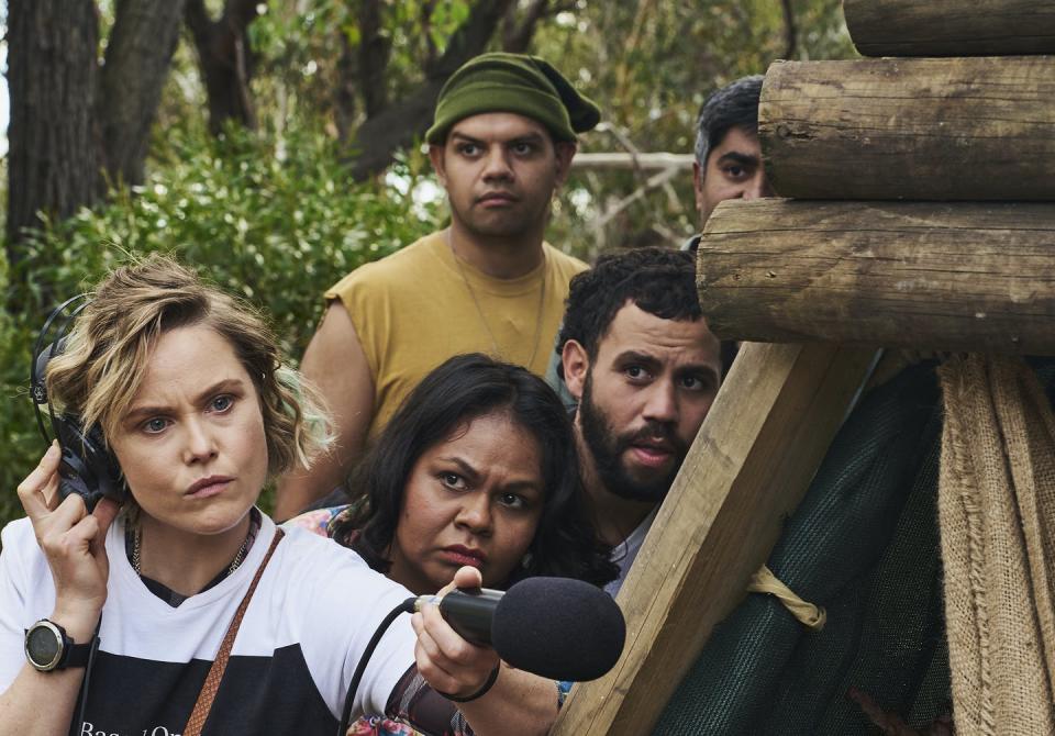 A white woman with a shotgun mike, looked on by three Aboriginal people.