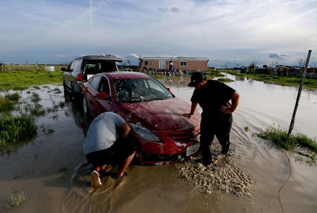 Jairo Estrada, left, and Juan Espinoza work to get one of their family's car off their flooded property in Allensworth.