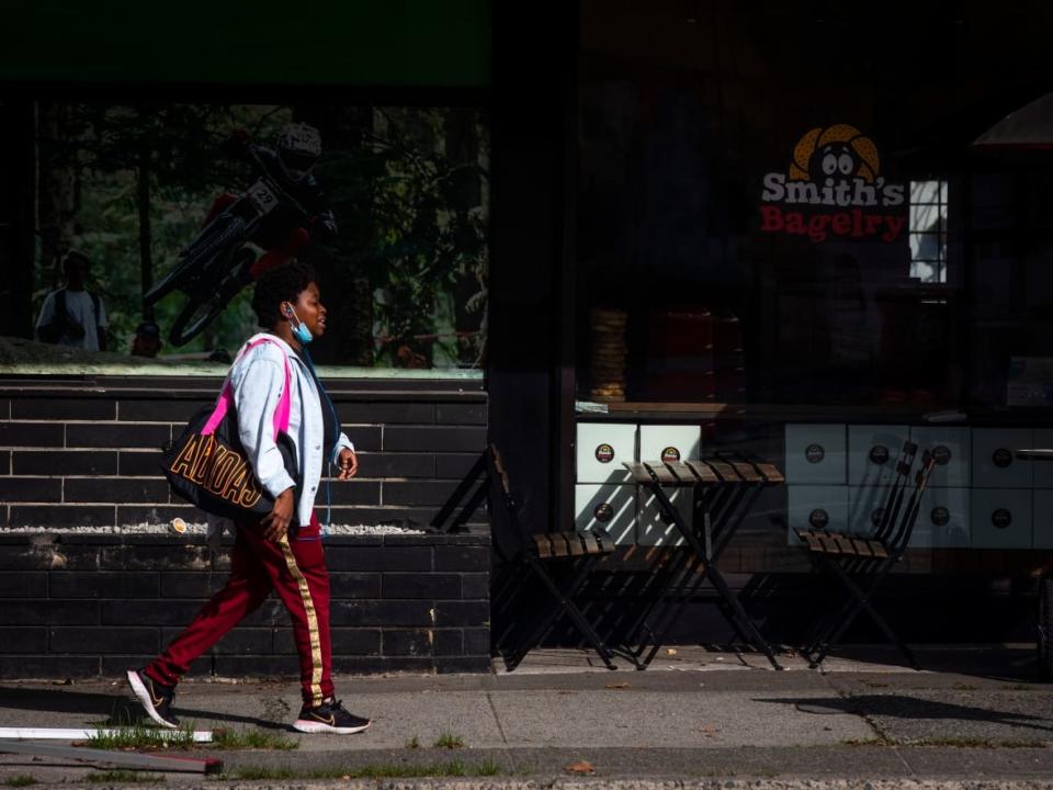 A pedestrian passes a restaurant patio with a face mask handy to protect against COVID-19 in Vancouver on Oct. 4. (Ben Nelms/CBC - image credit)