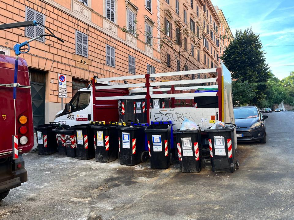 A line of trash cans behind a building in Italy