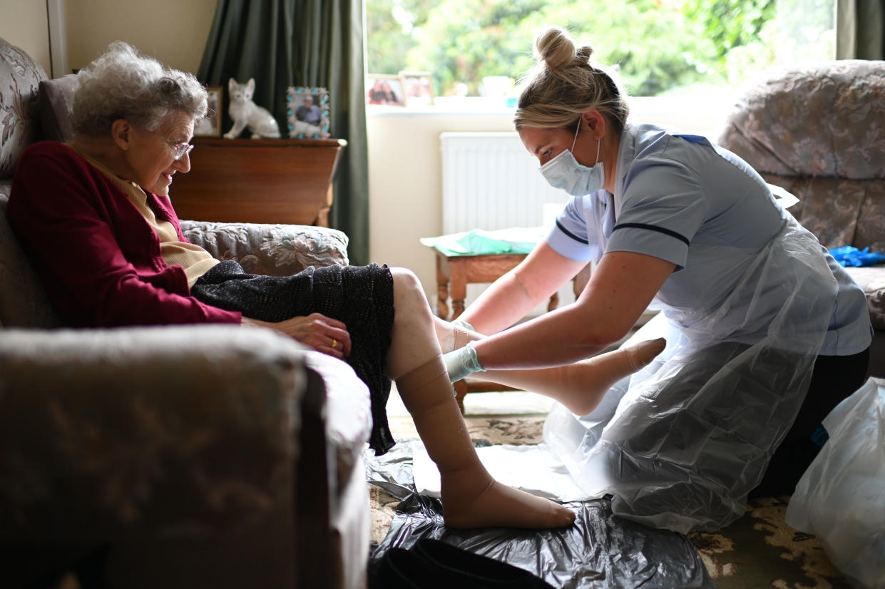 GRIMSBY, ENGLAND - JUNE 09: District nurse Rebecca McKenzie (R), wearing personal protective equipment (PPE) changes the dressings on the legs of 86-year-old Margaret Ashton (L) to treat her leg ulcers during a home visit on June 9, 2020 in Grimsby, northeast England. (Photo by Daniel Leal-Olivas - Pool/Getty Images)