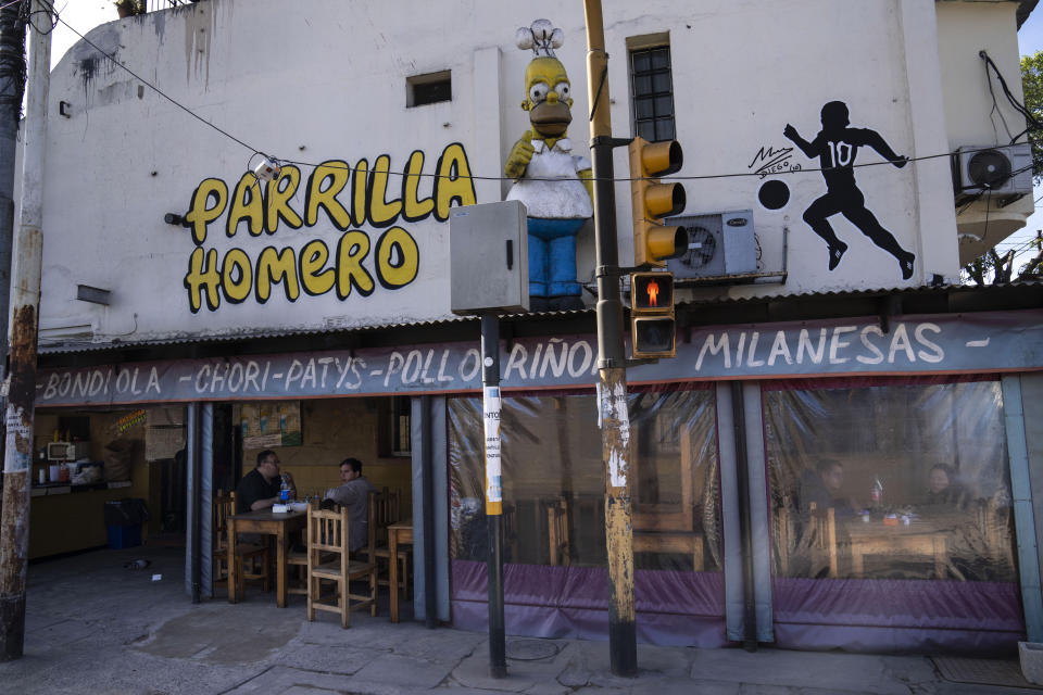 A sculpture of Homer Simpson flashing a thumbs up and wearing a chef's hat, stands on the top of an aluminum roof of the grill that bears the name of 'The Simpsons' protagonist, in Ciudadela, Argentina, Monday, Oct. 17, 2022. Waiters said that the owner of the business which serves cuts of grilled meat, brought the sculpture in a truck from the coastal city of Mar del Plata. (AP Photo/Rodrigo Abd)