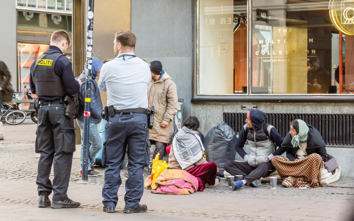 Two policemen looking at the documents of some immigrants, who are sitting on the street. Copenhagen, Denmark - Stig Alenas/Alamy Stock Photo