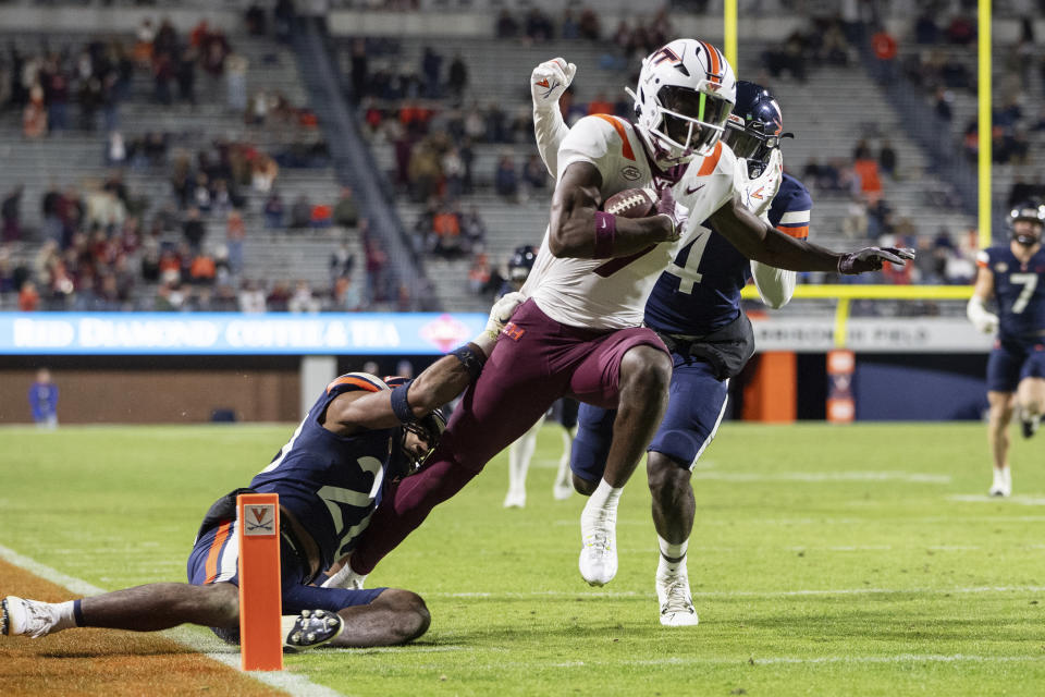 Virginia Tech wide receiver Da'Quan Felton, front center, scores a touchdown as he is tackled by Virginia safety Jonas Sanker, left, and cornerback Dave Herard, right, during the second half of an NCAA college football game Saturday, Nov. 25, 2023, in Charlottesville, Va. (AP Photo/Mike Caudill)