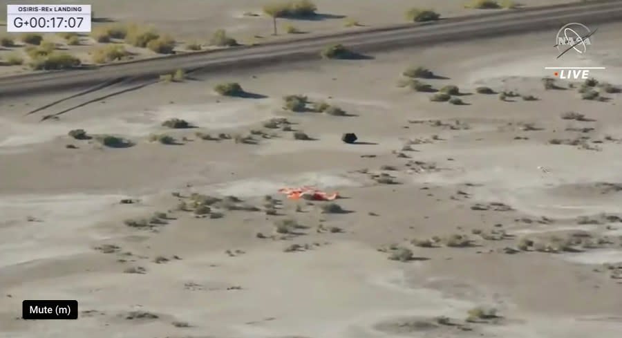 This image taken from video provided by NASA TV shows the capsule released by the Osiris-Rex spacecraft lying on the surface near the parachute after landing to Earth, Sunday Sept. 24 2023. (NASA TV via AP)