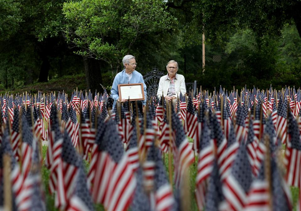 Kathy Wash sits alongside Ellie Sukkestad among some of the 26,000 flags on display in the garden at the National Museum of the Mighty 8th Air Force on Friday, May 26, 2023. Walsh holds a Purple Heart certificate for her uncle, George Hayes, who was killed over Belgium during WWII.
