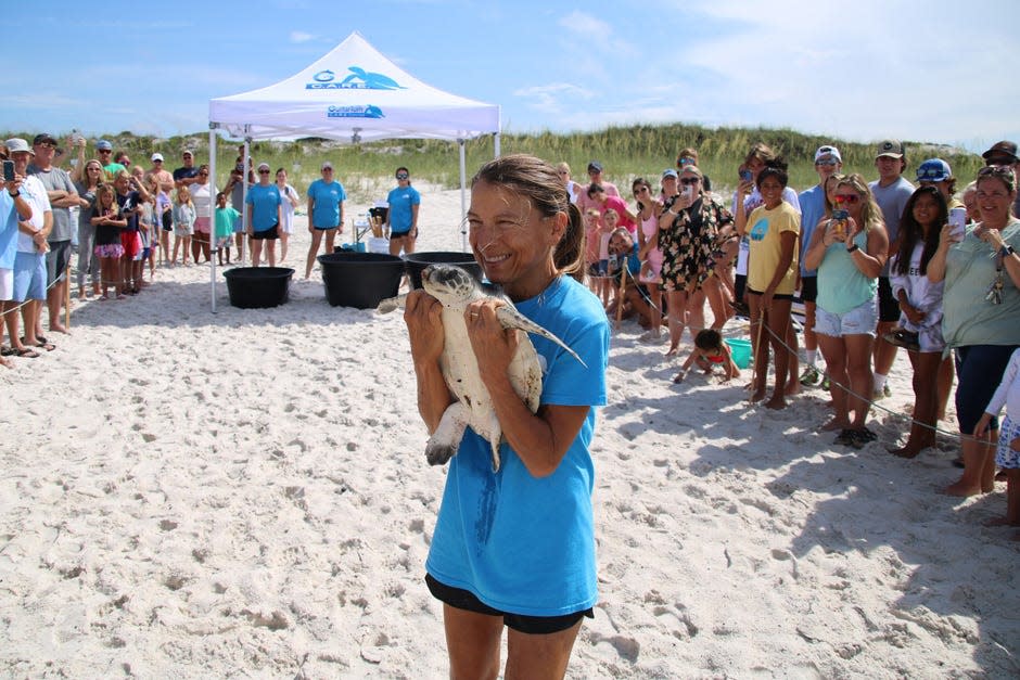 Crowds watch as C.A.R.E. volunteer Christi carries Silvia towards the Gulf of Mexico June 29 at Inlet Beach.