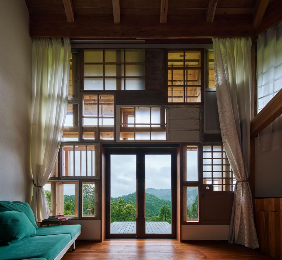 Inside the windowed building overlooking lush mountains on a cloudy day with a green couch in the foreground