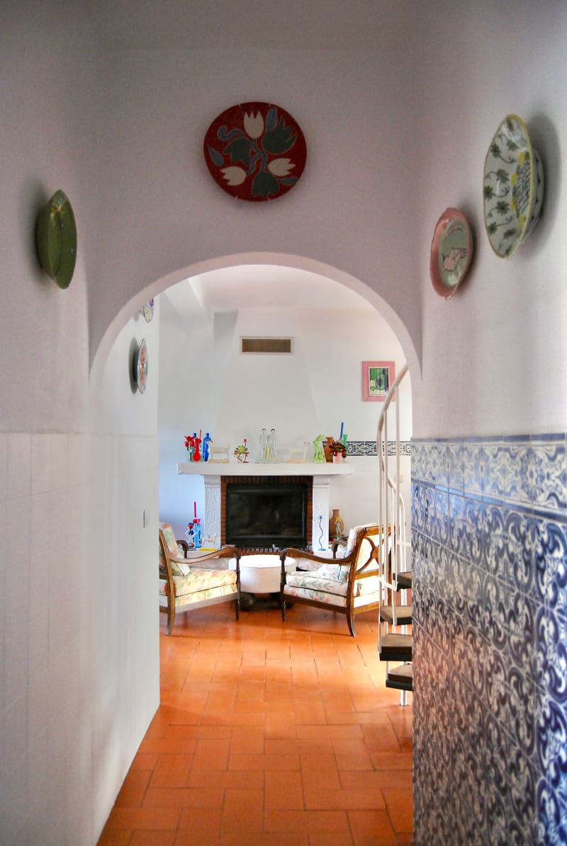 Chairs in front of fireplace seen from hallway with white walls and blue tile.