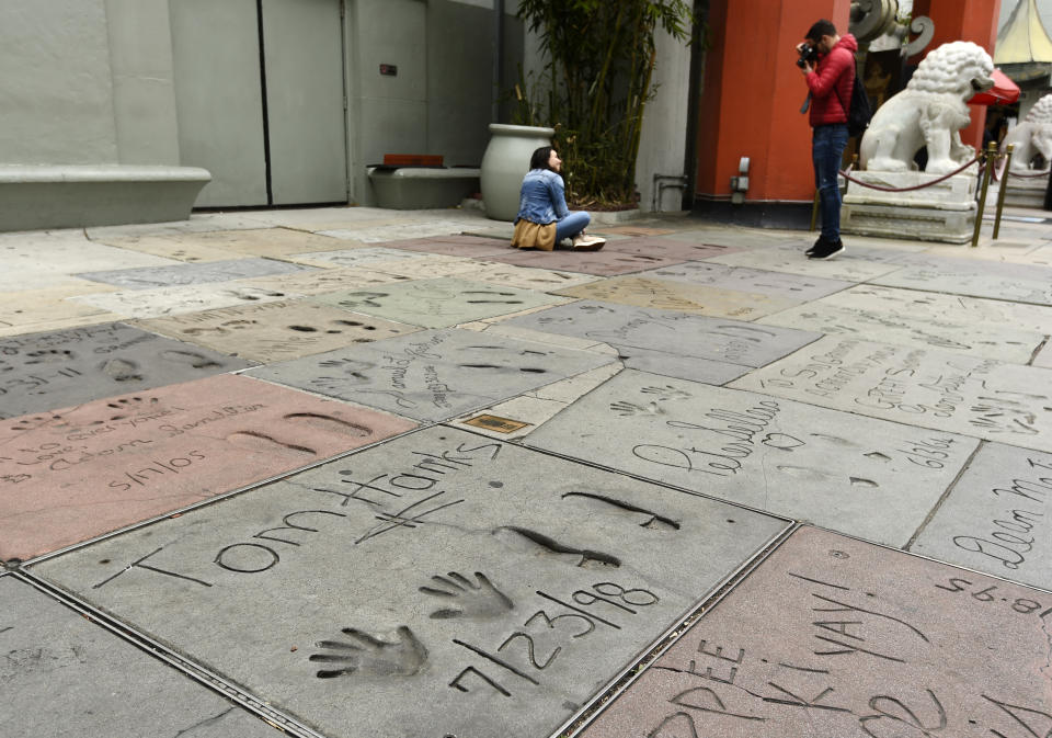 Visitors take pictures near the cement inscription of actor Tom Hanks in the forecourt of the TCL Chinese Theatre, Thursday, March 12, 2020, in the Hollywood section of Los Angeles. Hanks and his wife, actress-singer Rita Wilson, have tested positive for the coronavirus, the actor said in a statement Wednesday. For most people, the new coronavirus causes only mild or moderate symptoms. For some it can cause more severe illness. (AP Photo/Chris Pizzello)