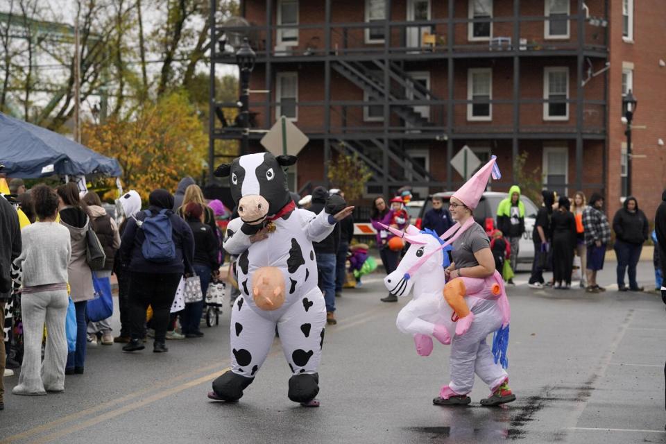People dressed up as a cow and a unicorn rider dance next to a crowd in a street