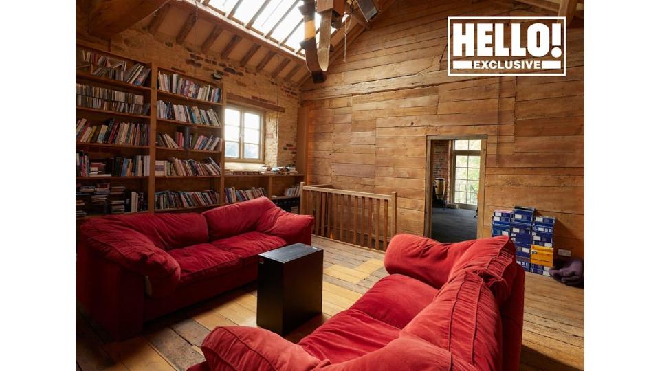 Blur star Alex James's library room at farmhouse in Kingham, Oxfordshire featuring wood panelled walls and red sofas  