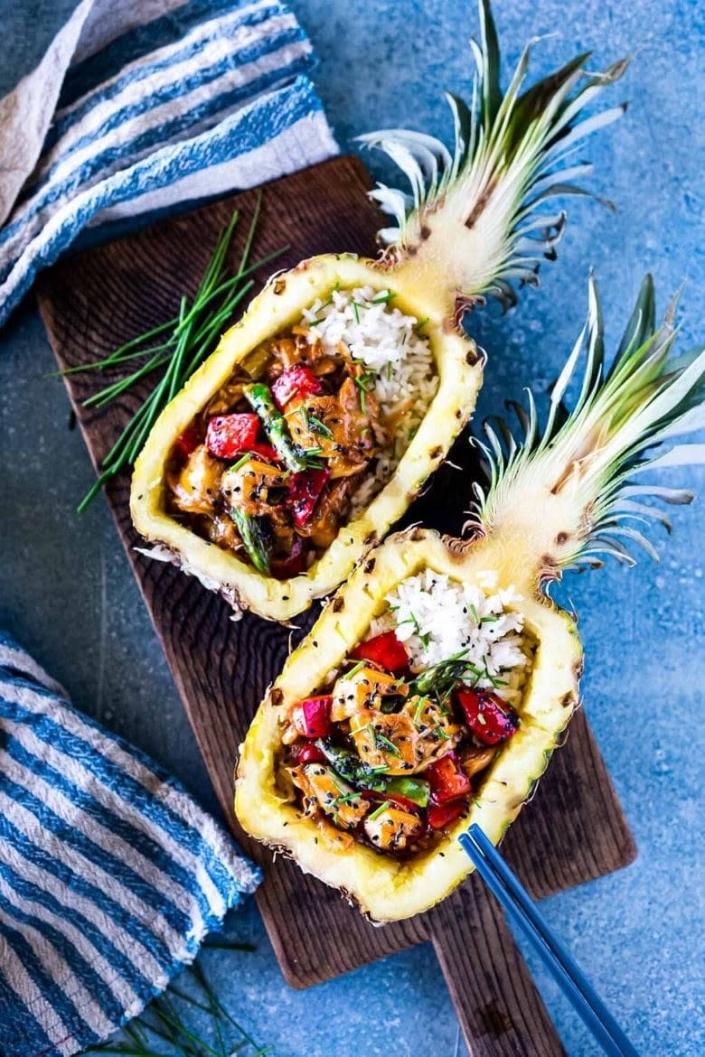 Halved and hollowed out pineapple with rice, chicken, and vegetables with chopsticks. 