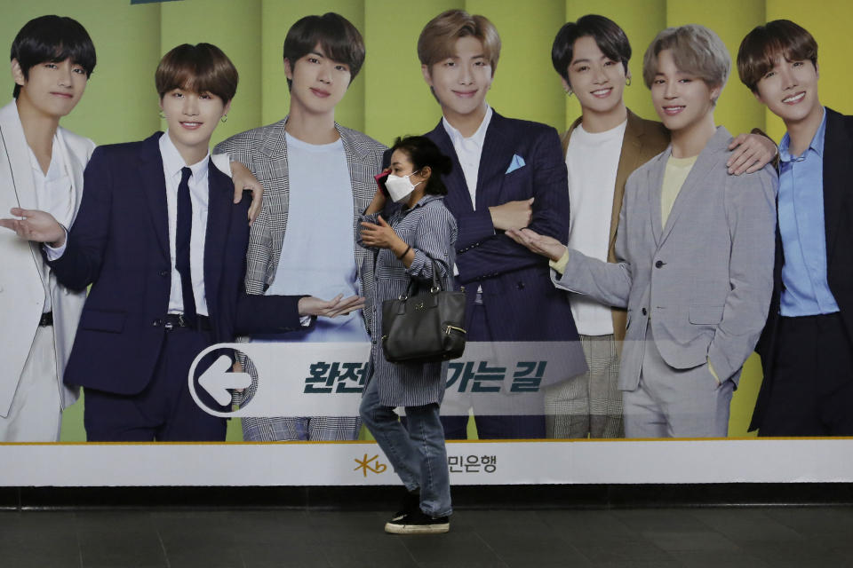 A woman wearing a face mask to help protect against the spread of the coronavirus walks by a board showing members of South Korean K-Pop group BTS to advertise a local bank's money exchange in Seoul, South Korea, Wednesday, Sept. 30, 2020. (AP Photo/Ahn Young-joon)