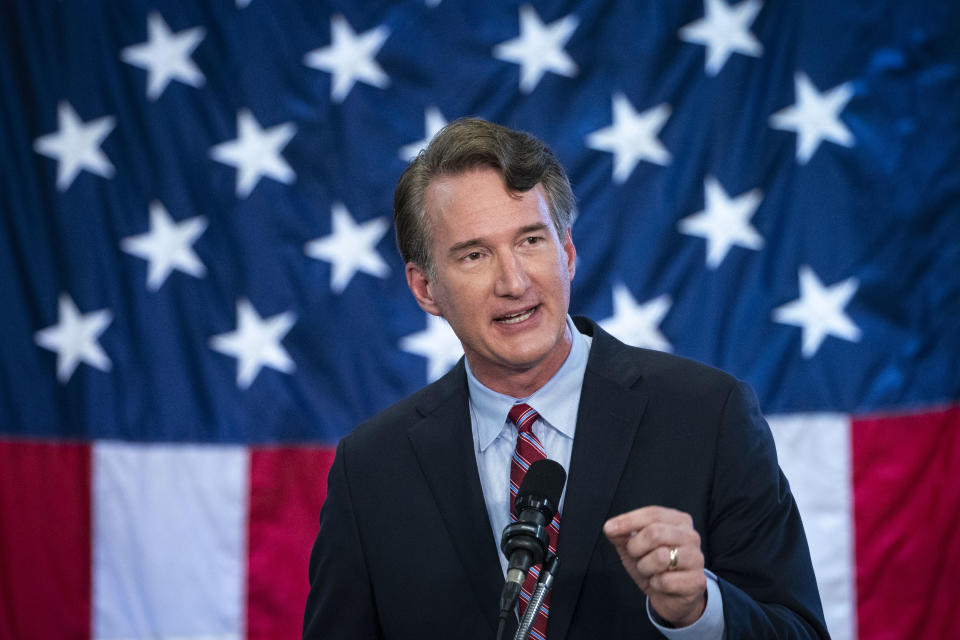 Glenn Youngkin speaks before a microphone in front of an American flag.