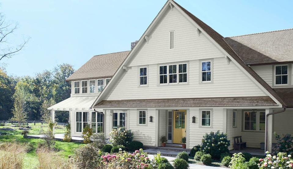 A two story house is painted in a creamy off white and surrounded by green landscaping.