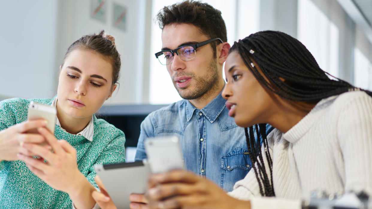 Diversity group of young male and female creative designers collaborating on new business project and searching information on modern smartphones and using digital tablet for productive work.