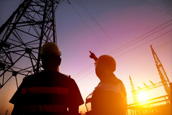 Two worker watching the power tower and substation with sunset background.