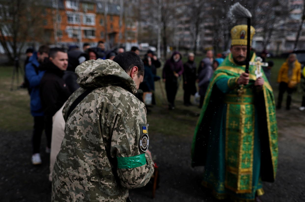 An Orthodox priest sprinkles holy water on worshippers outside.