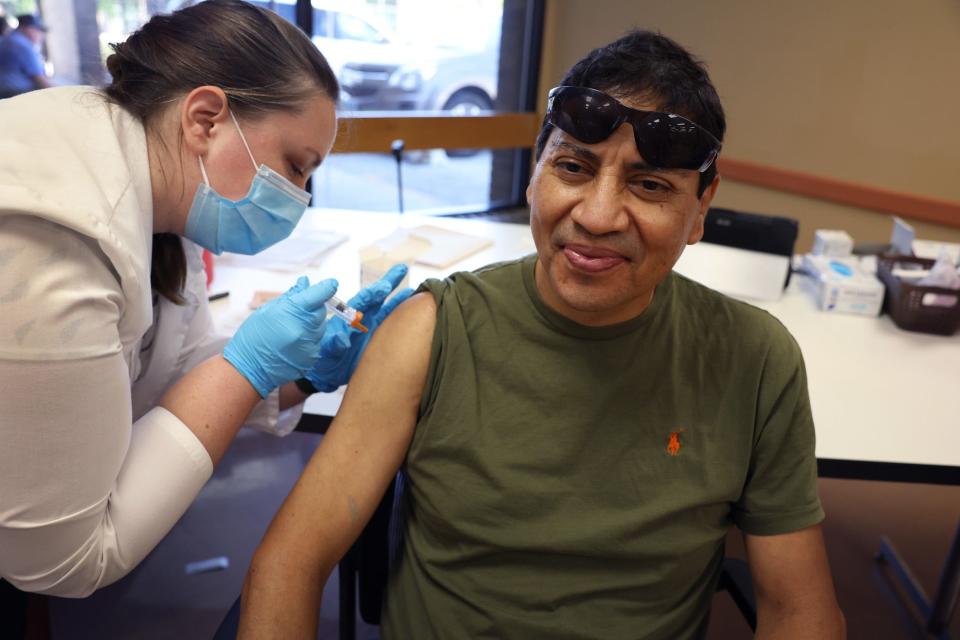 picture of man sitting down, smiling, getting his flu shot injected by pharmacist who is wearing a mask.