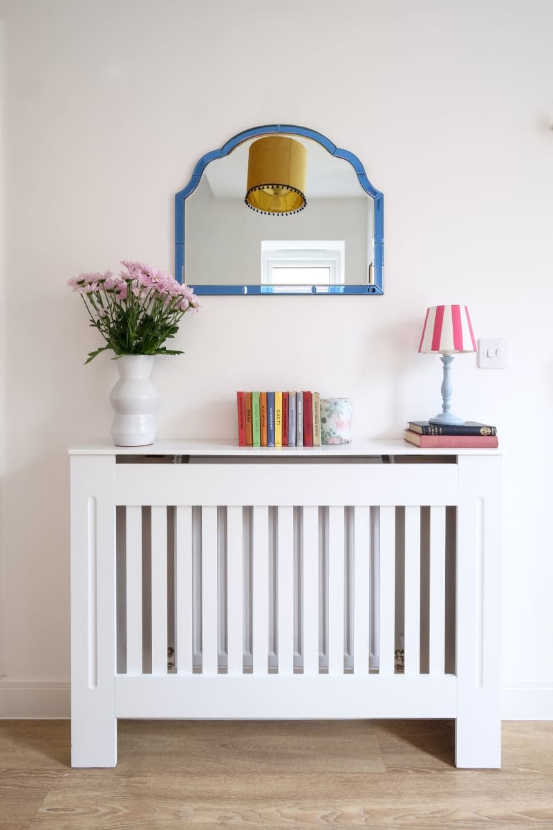blue frame vintage shaped mirror above white slated table with pink and white striped lamp shade and colorful books