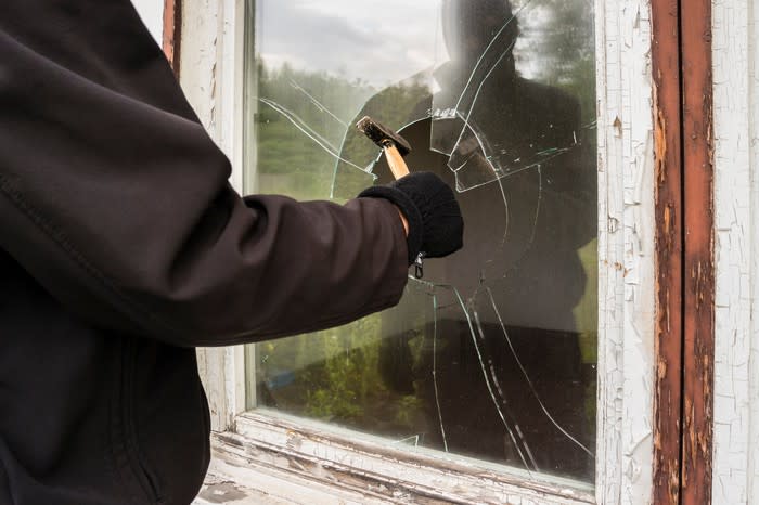 身穿黑色外套的人用錘子敲破窗子。
