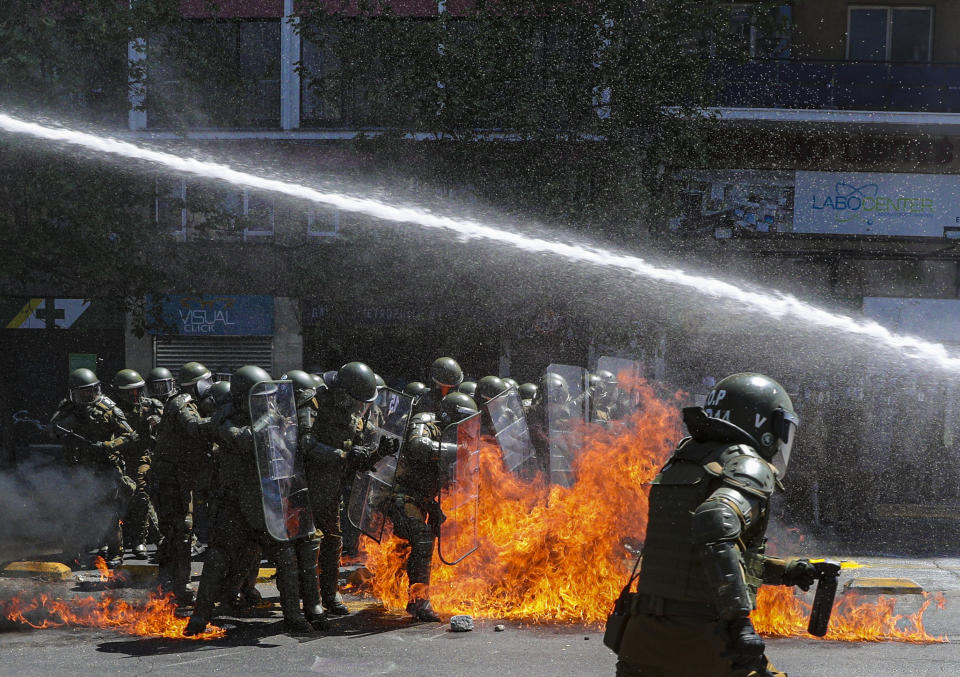 Fire from a molotov cocktail explodes in front of police as a police vehicle shoots water at protesters who marched against the commemoration of the discovery of the Americas, organized by Indigenous groups demanding autonomy and the recovery of ancestral land in Santiago, Chile, Monday, Oct. 12, 2020. (AP Photo/Esteban Felix)