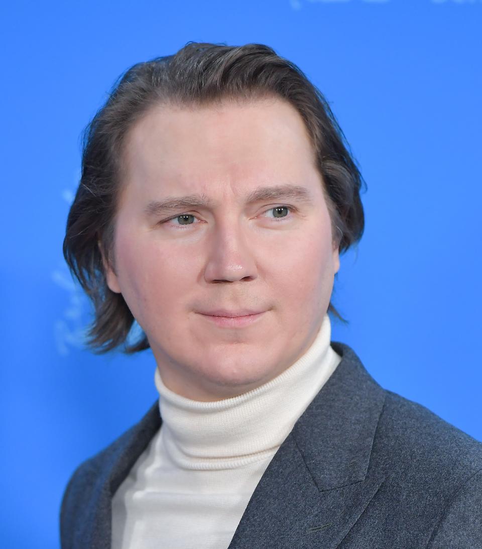 a man in a turtleneck sweater and sports coat stands on a red carpet