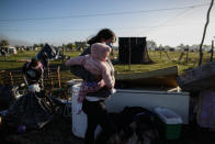 A woman carries a baby amid her belongings and destroyed shack as police evict people from a squatters camp in Guernica, Buenos Aires province, Argentina, Thursday, Oct. 29, 2020. A court ordered the eviction of families who are squatting here since July, but the families say they have nowhere to go amid the COVID-19 pandemic. (AP Photo/Natacha Pisarenko)