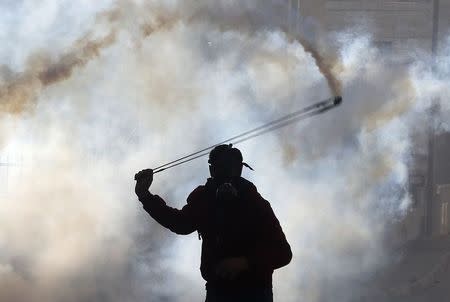 A Palestinian protester uses a slingshot to throw back a tear gas canister fired by Israeli troops during clashes, following the funeral of Palestinian minister Ziad Abu Ein near the West Bank city of Ramallah December 11, 2014. REUTERS/Ammar Awad