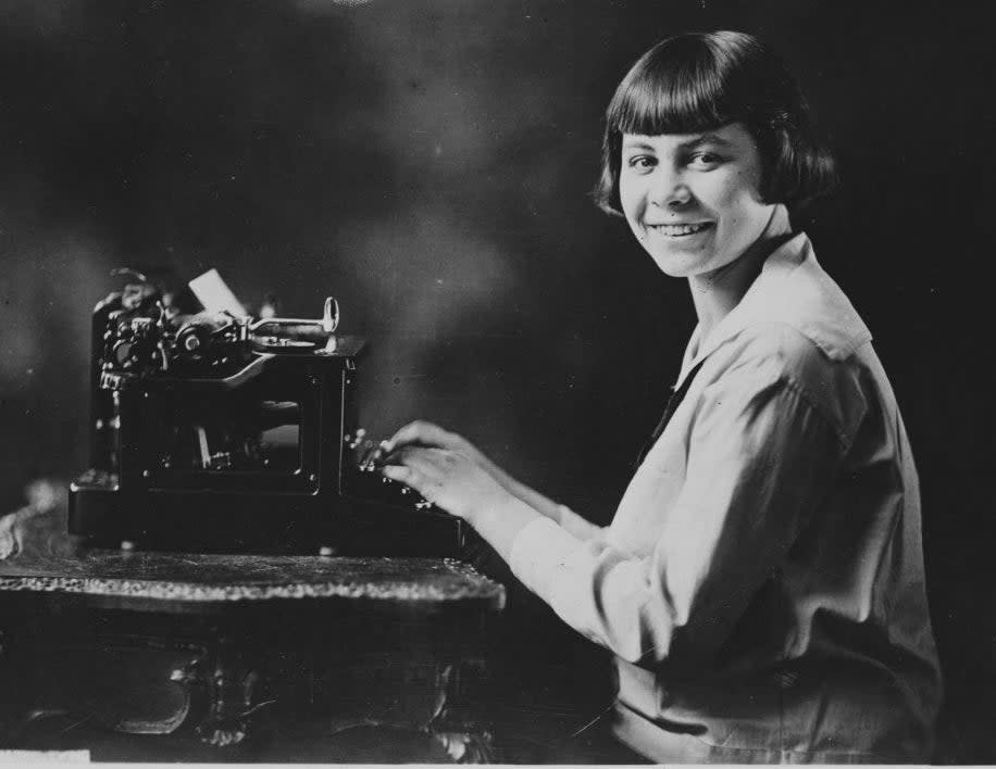 A teen in 1920 sits before a large typewriter