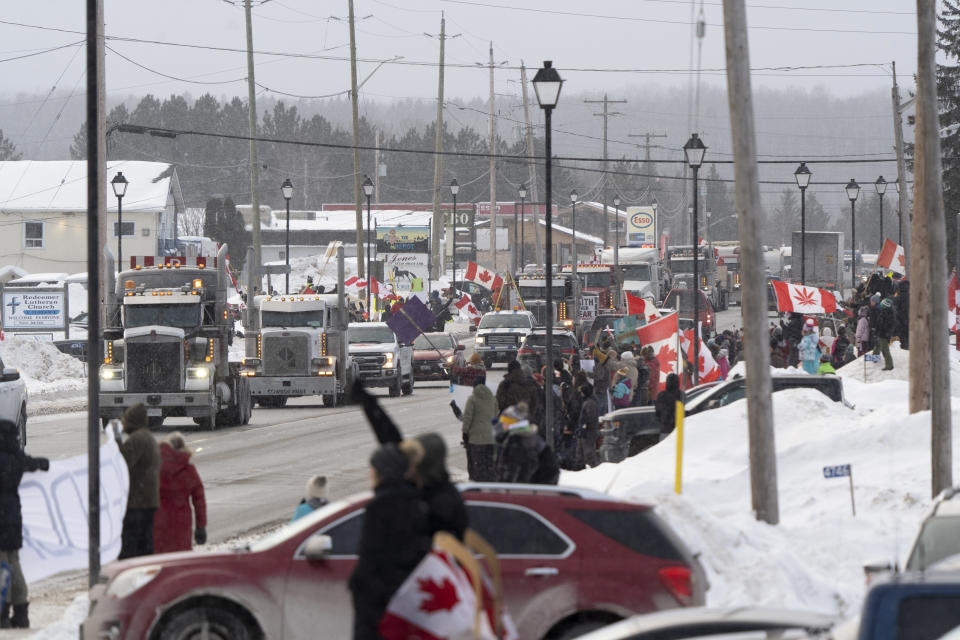 Protesters and supporters against a COVID-19 vaccine mandate for cross-border truckers cheer as a parade of trucks and vehicles pass through Kakabeka Falls outside of Thunder Bay, Ontario, on Wednesday, Jan. 26, 2022. (David Jackson/The Canadian Press via AP)