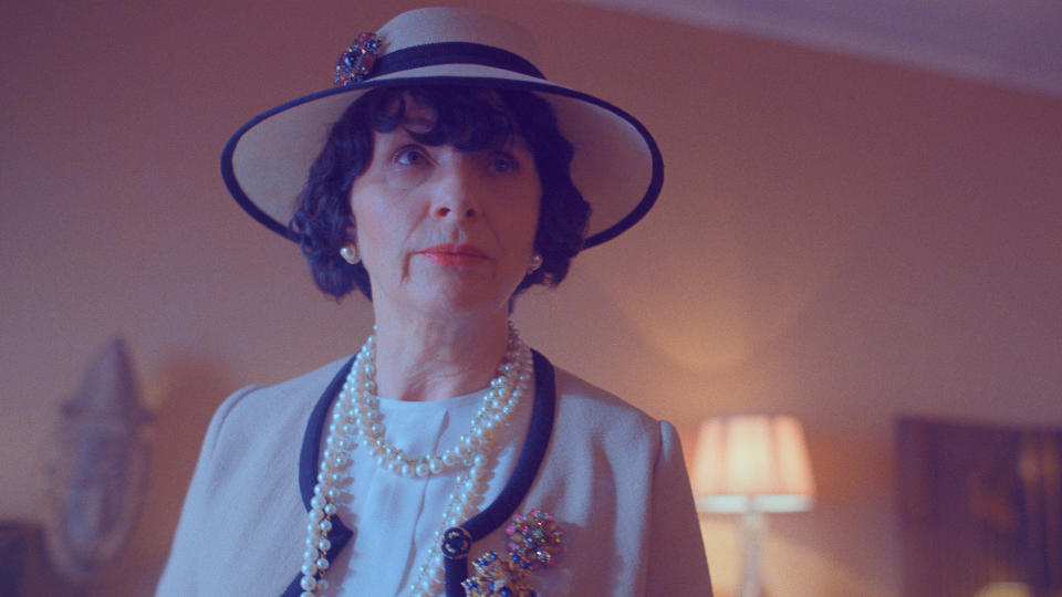 A woman in a beige cardigan and matching hat, wearing a pearl necklace; Juliette Binoche as Coco Chanel in "The New Look"